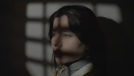 cinematic close-up of a woman standing indoors, her face partially illuminated by light filtering through a window