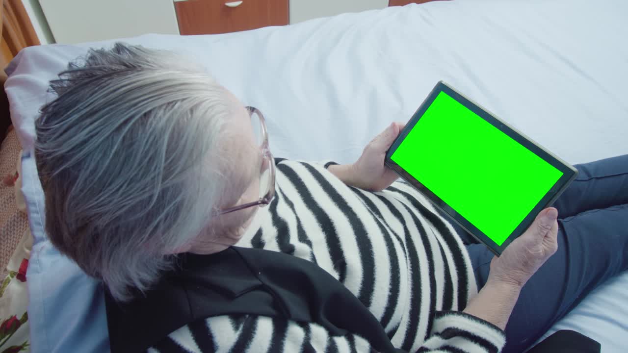 노인 여성 은 침대 에 누워 있는 태블릿 pc 를 통해 전자 책 을 읽는다