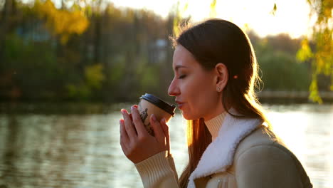 Woman enjoying coffee in an autumn park by the lake at sunset