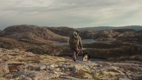 hiker with his pet dog walking in hildremsvatnet lake in norway - wide shot