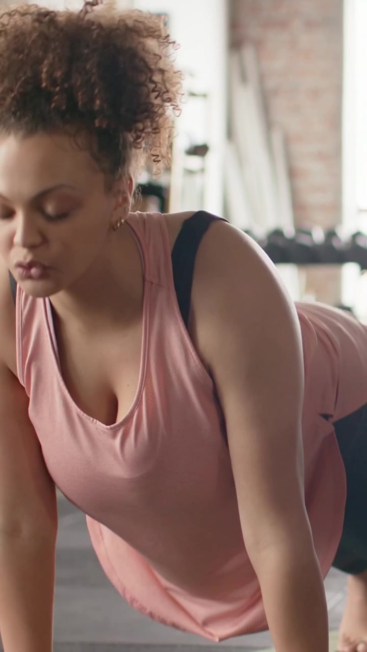 Vertical video: Inhaling woman in pink tank on mat at gym, flowing plank-to-dog-to-lunge for yoga