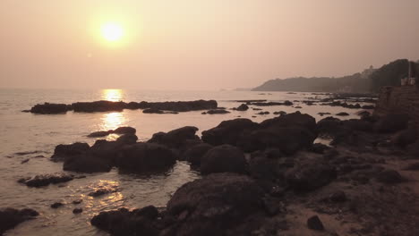 rocas durante la puesta de sol en la costa de la playa goa india en la india trópico goa en la bahía del mar arábigo océano indio puesta de sol de la playa aérea cinematográfica pan hacia atrás movimiento