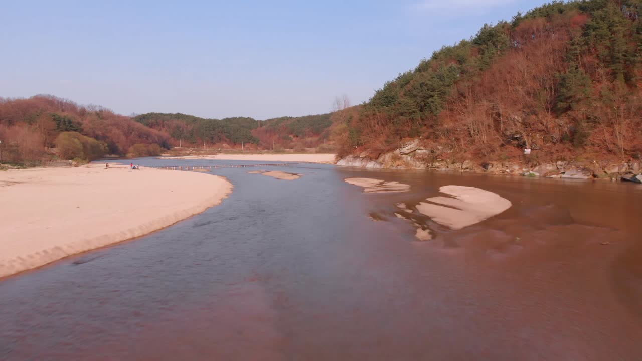 Aerial approach above river towards tiny wooden bridge