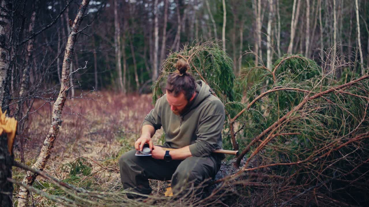A Man Sharpening An Axe In The Woods. Static Shot