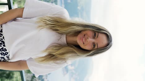 Blonde-woman-looks-at-the-camera-standing-on-the-background-of-beautiful-mountains