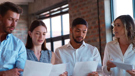 Smiling-Multi-Cultural-Business-Team-Standing-Together-Meeting-Discussing-Paperwork-In-Modern-Office