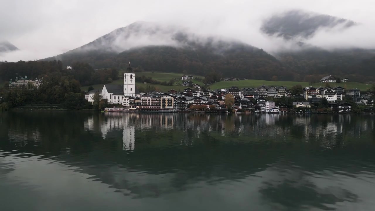 Bewegte Drohnenaufnahme aus der Luft von Wolfgang am Wolfgangsee aus der Ferne an einem regnerischen Tag nahe dem See