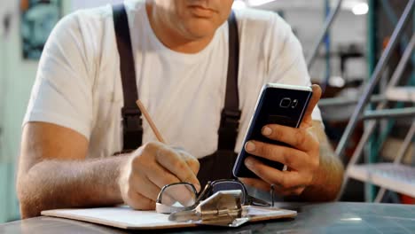 male mechanic writing on clipboard while using mobile phone 4k