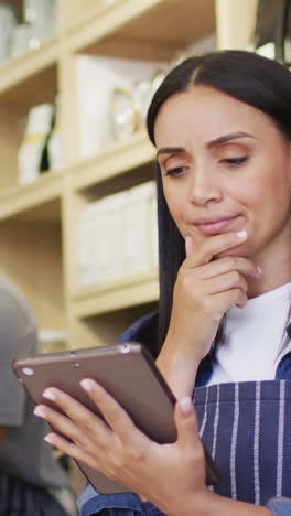 animation of thoughtful biracial waitress using tablet in coffee shop