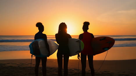 three surfers silhouetted against a sunset beach