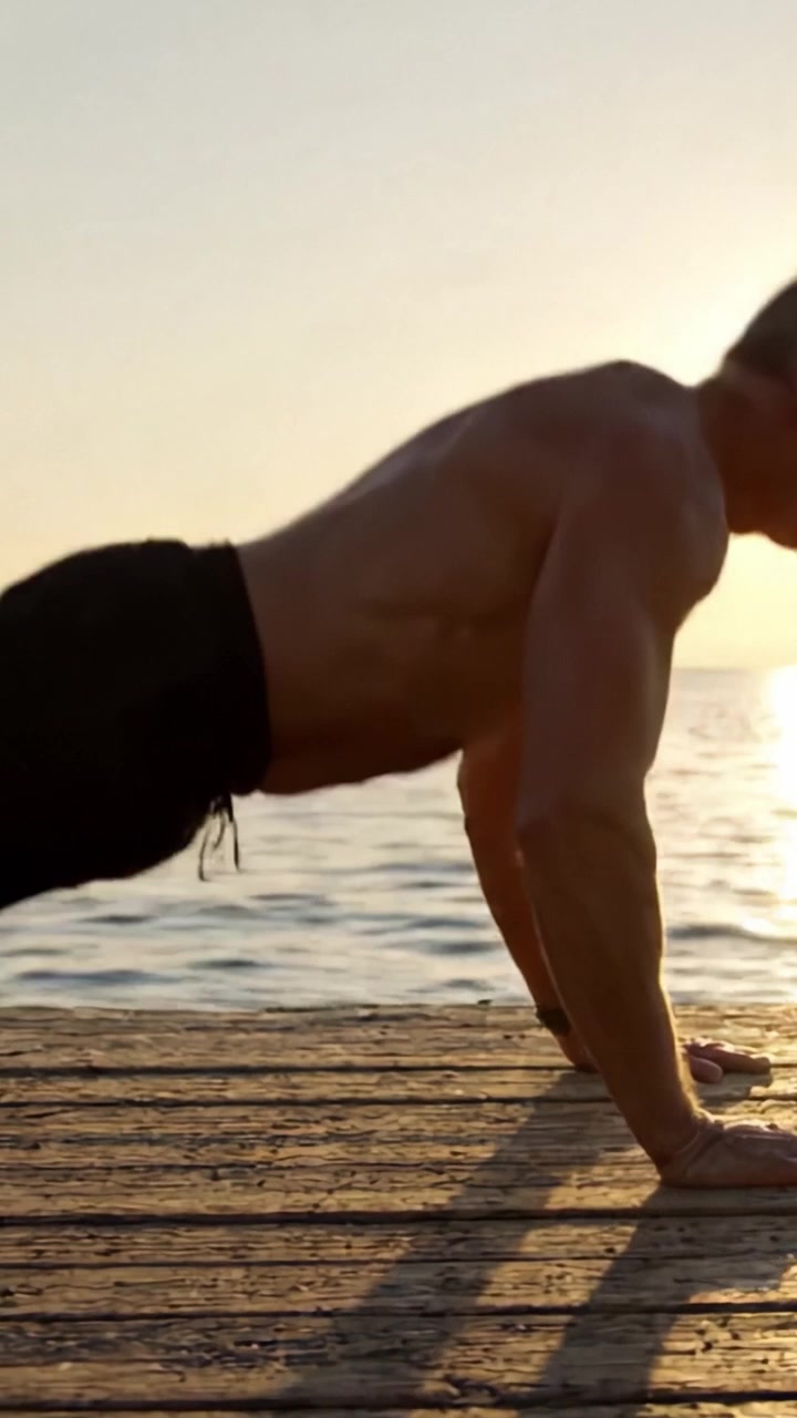 Un individuo in forma si impegna in esercizi di flessioni su un molo al tramonto, mostrando forza, dedizione e la bellezza del fitness all'aperto
