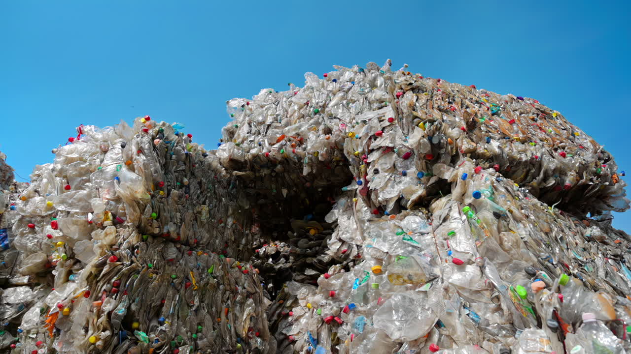 Multiple stacks of compressed transparent plastic garbage at waste recycling factory in open air. Slow motion
