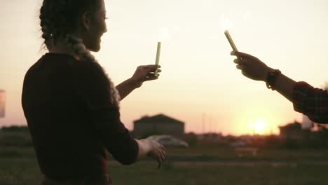 back view of smiling friends having fun waving with firework candles during sunset