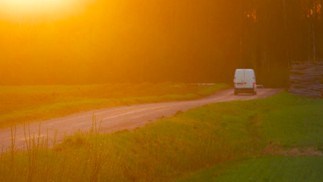 cars drive on dusty countryside gravel road during bright sunset, latvia