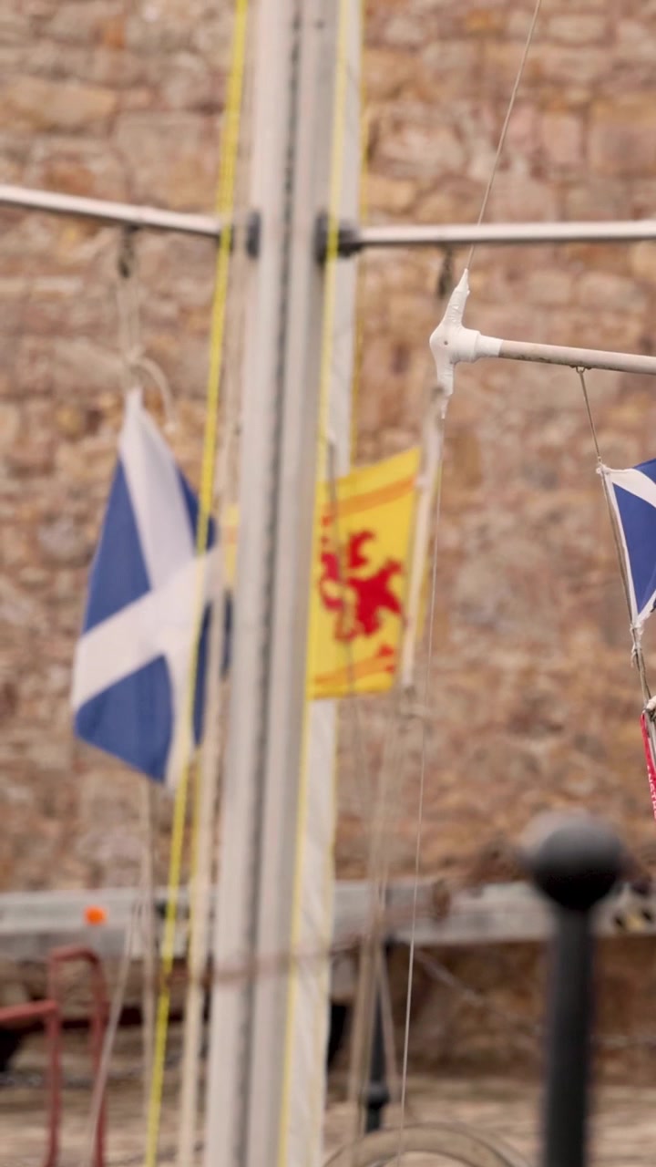 Close-up of blue and yellow Scottish flags fluttering on a mast against stone walls.