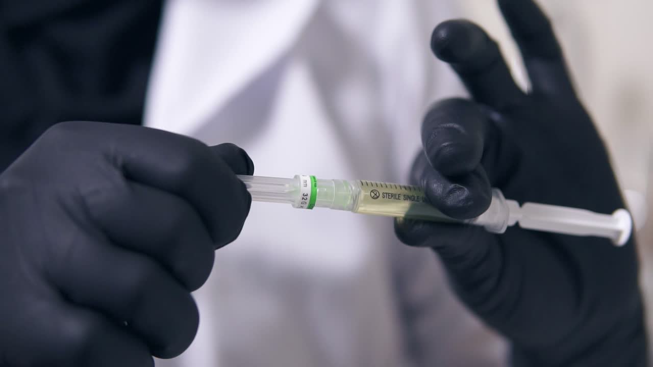 Closeup view of professional doctor's hands in black gloves with medical syringe in hands, getting ready for injection