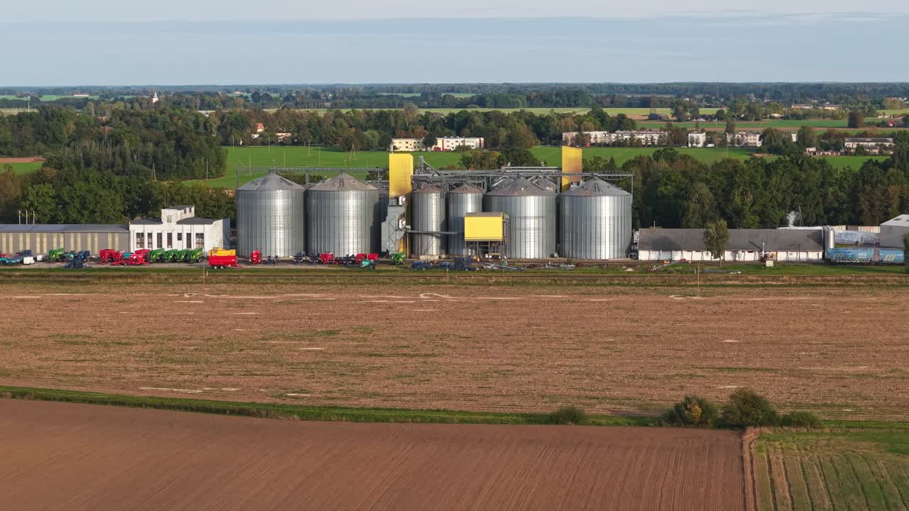 Wide of grain processing facility with silos and trucks on flat agricultural land