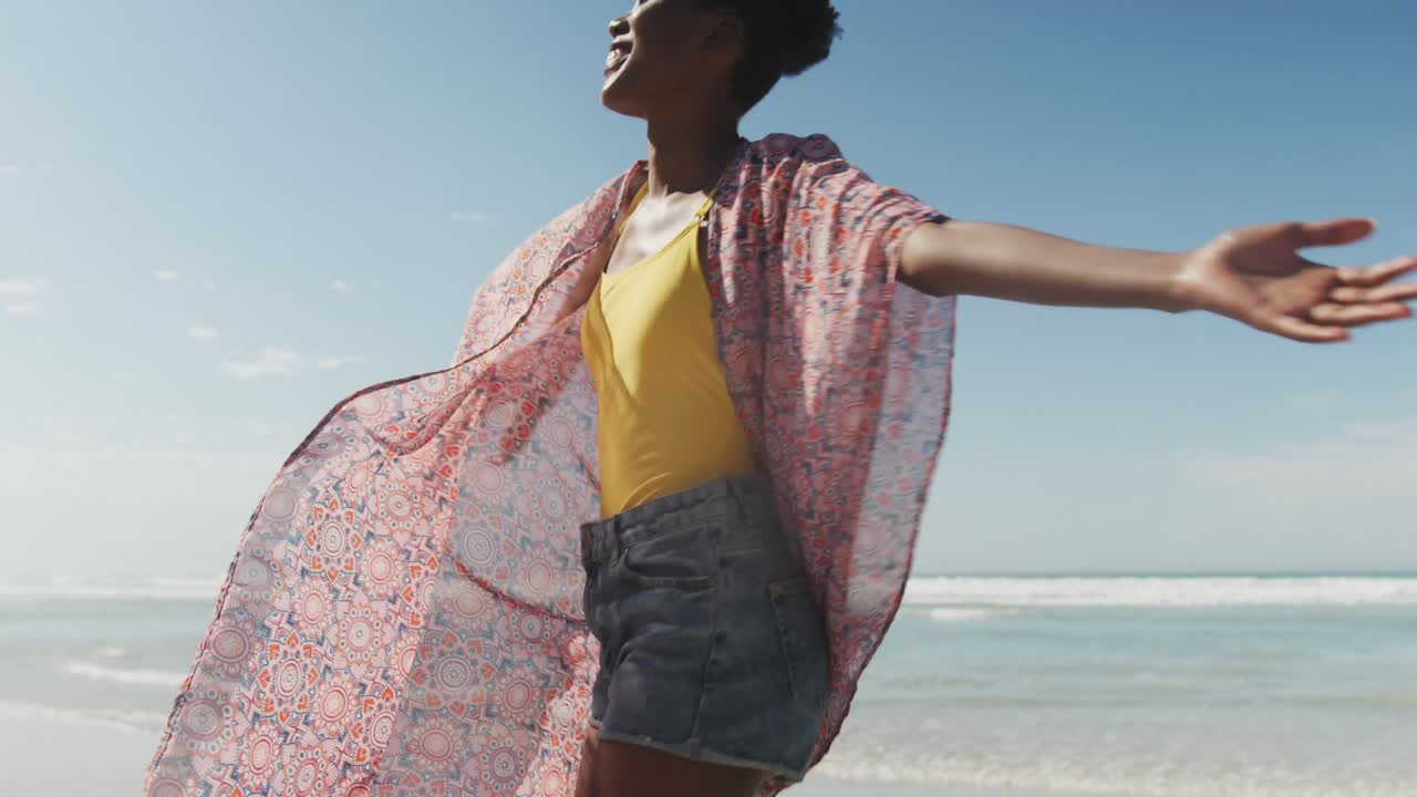 feliz mujer afroamericana con los brazos abiertos en una playa soleada