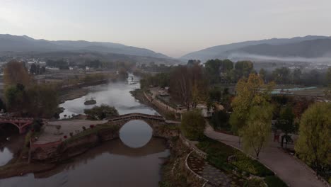 Traditional-old-Chinese-town-stone-arch-bridge-over-river,-aerial-view
