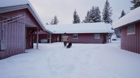 Man-With-His-Alaskan-Malamute-Dog-Near-Cabins-In-Indre-Fosen,-Norway-During-Winter---wide