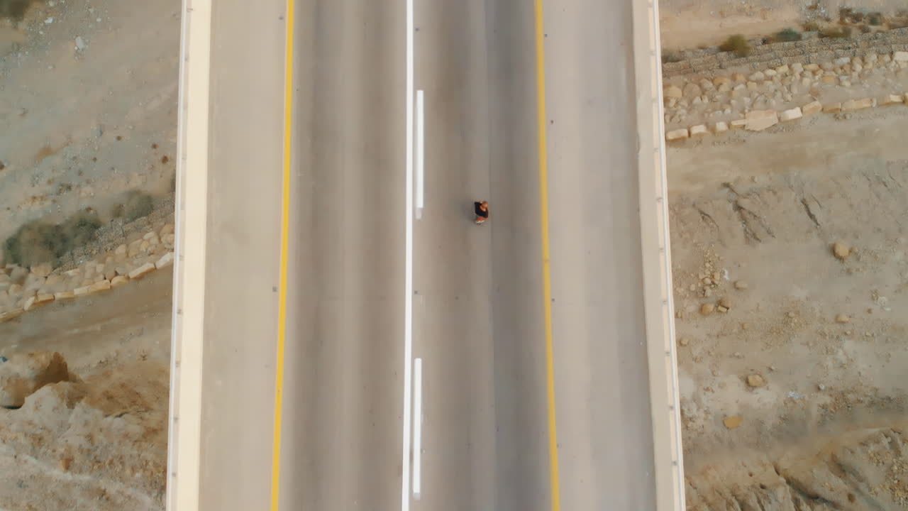 남자는 자동차가 지나가는 동안 거대한 다리에서 카버 스케이트 보드를 혼자 탄다.