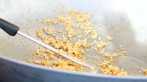 persona preparando un bocadillo de fideos crujientes en un gran wok al aire libre