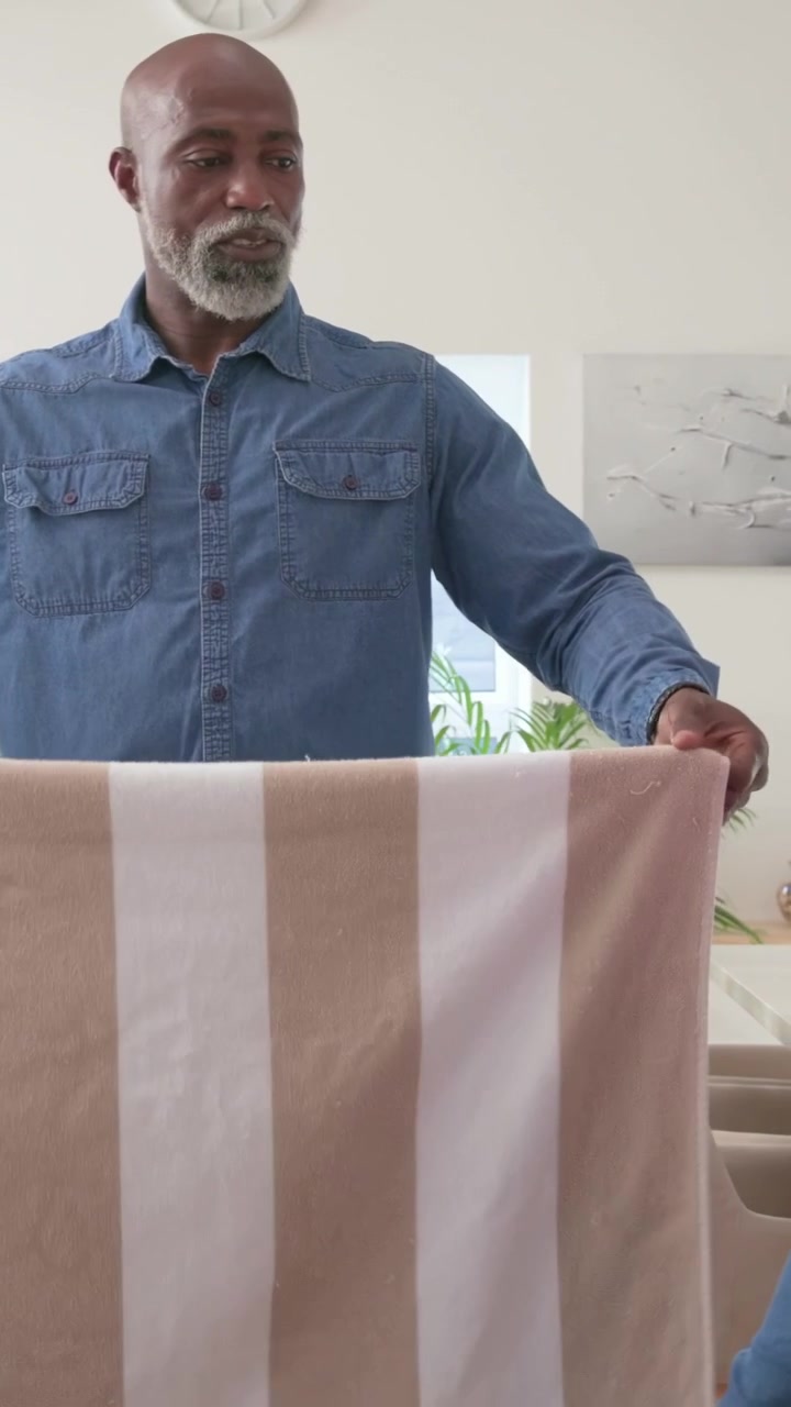 Vertical video: Taking towel from basket, man folding striped towel at dining table, giving to girl