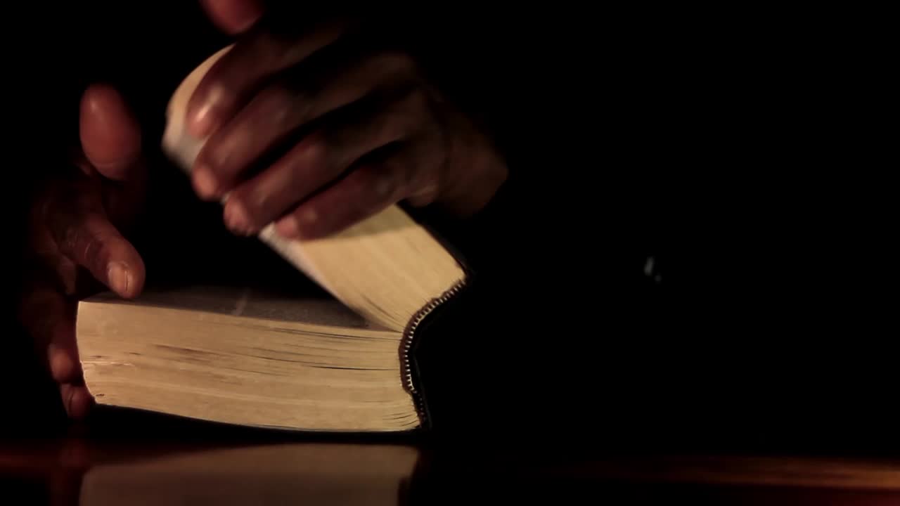 Homme caribéen priant Dieu, les mains jointes, avec une bible et une croix, sur fond noir. Vidéo de stock