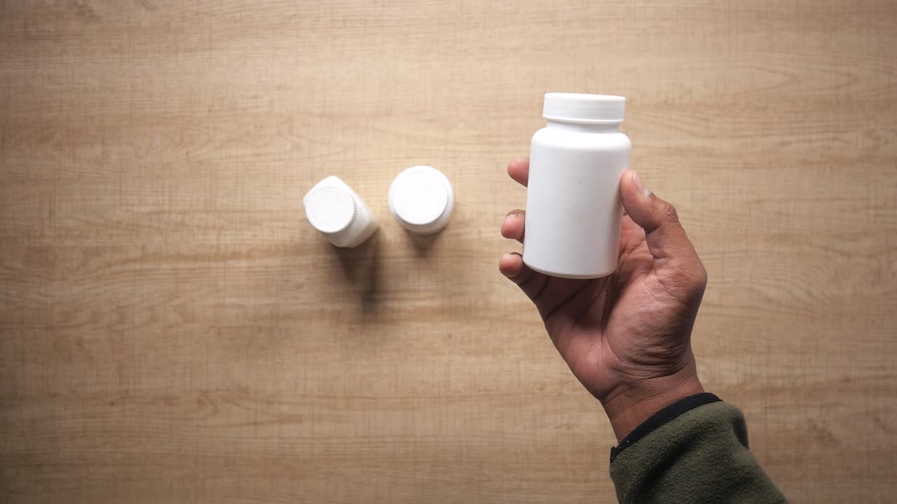 Hand holding a white pill bottle on a wooden table