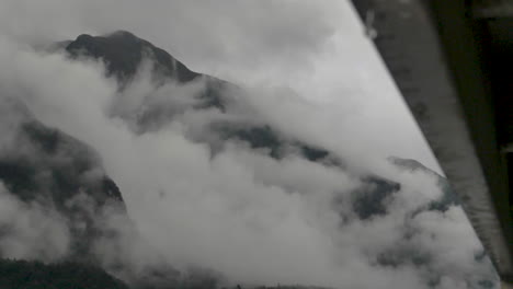 slow motion rain drops fall off side of boat in foreground with focus on cloudy mountains behind - doubtful sound , new zealand