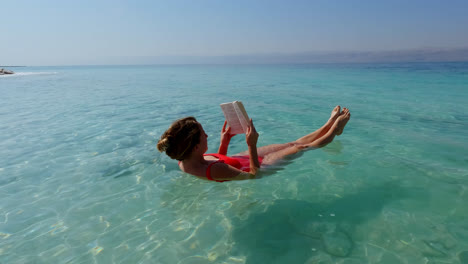 Friedliche-Junge-Frau,-Die-Im-Toten-Meer-Schwimmt,-Einen-Roten-Badeanzug-Trägt-Und-Ein-Buch-Liest