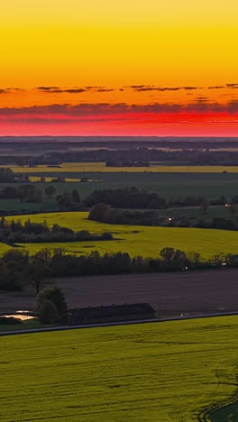 drone hyperlapse of glowing orange sunset sky above yellow canola fields, vertical