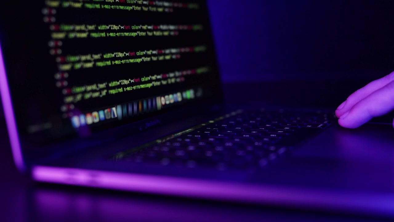 Close up of hand scrolling on a laptop mouse with coding on screen in a dark neon lid room.
