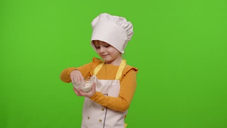 child girl kid dressed cook chef baker in apron and hat stir the flour in a plate, fooling around