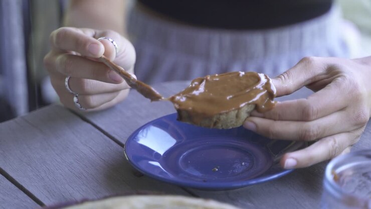 Close up female spreading sweet on bread, jam and knife on wooden table outdoors breakfast slow motion and 60fps
