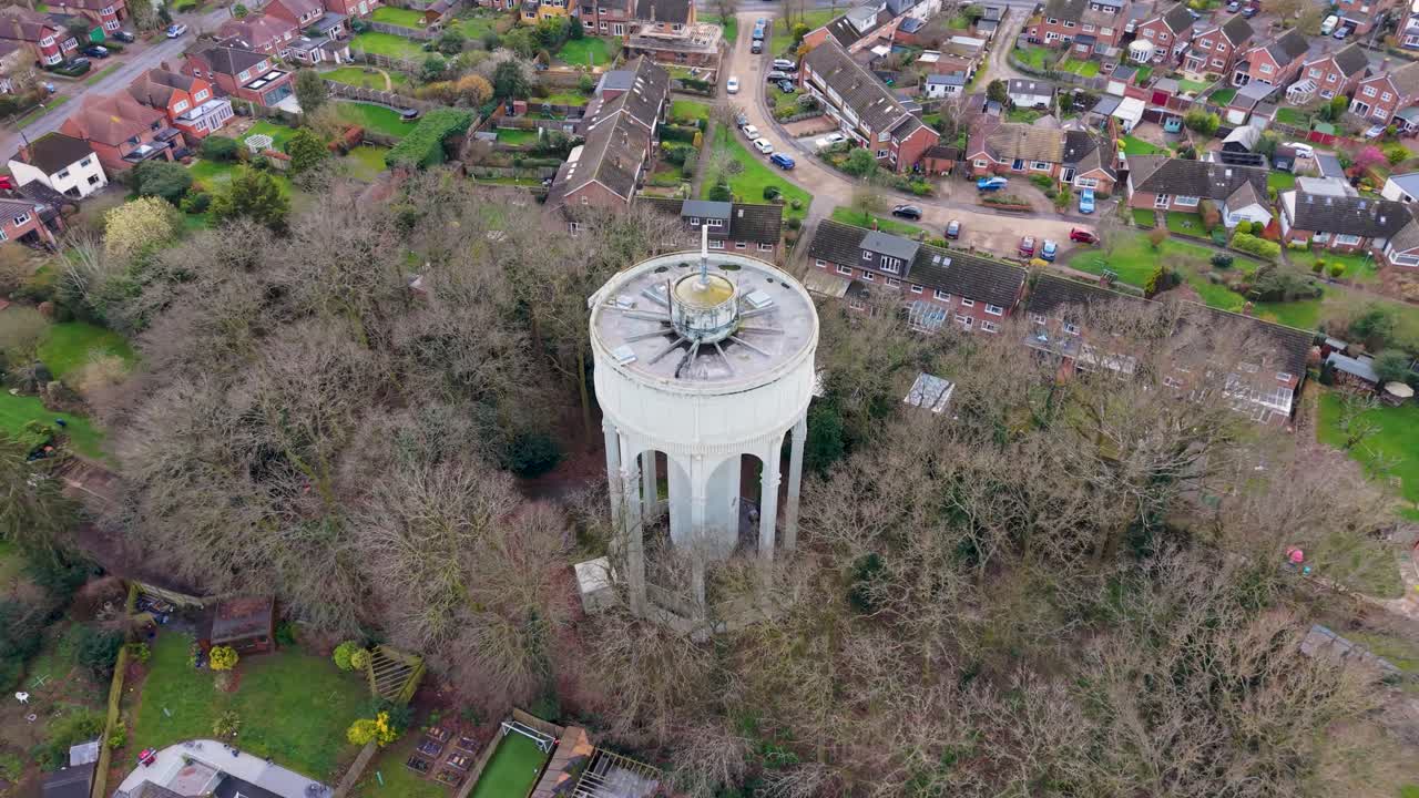 Drohnen-Orbit des Bengeo Wasserturms in Hertfordshire, UK, der sich nach links senkt, um winterliche Baumwipfel, Vorstadthäuser, Gärten und geschwungene Straßen in einer ruhigen Luftaufnahme zu enthüllen.
