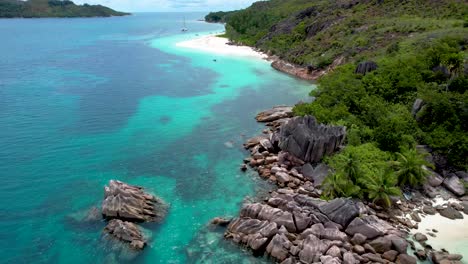 Luftaufnahme-Der-Felsigen-Küste-Auf-Der-Insel-Der-Seychellen-Mit-Verankertem-Boot-Und-Frau,-Die-Am-Abgelegenen-Strand-Spazieren-Geht