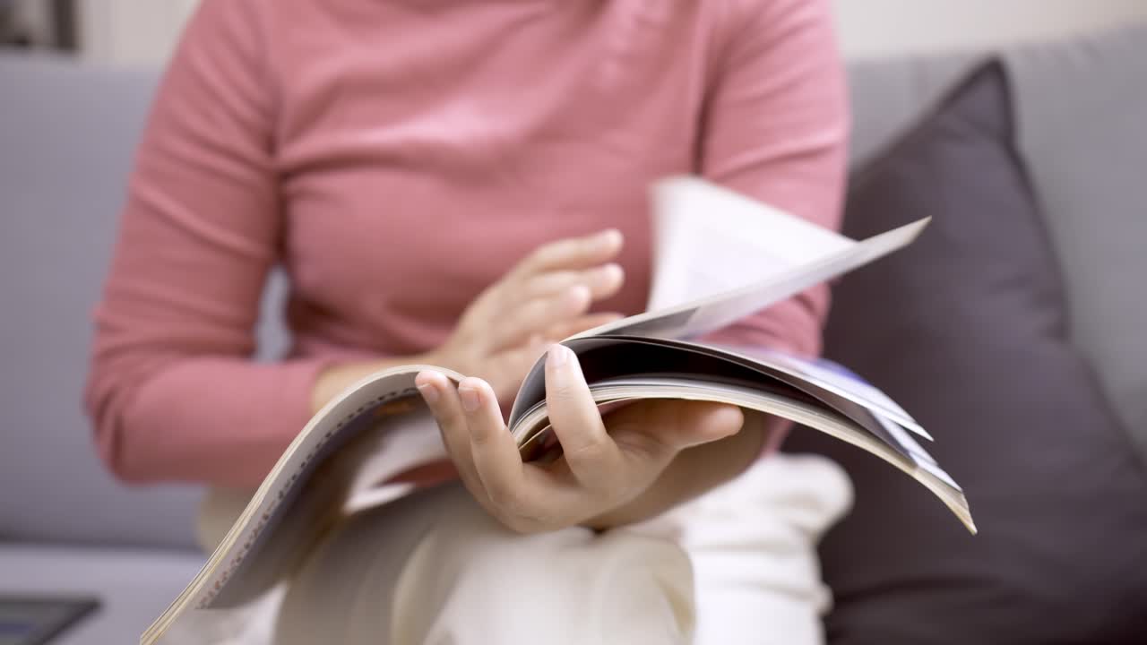 detalle de una mujer hojeando una revista sentada en un sofá
