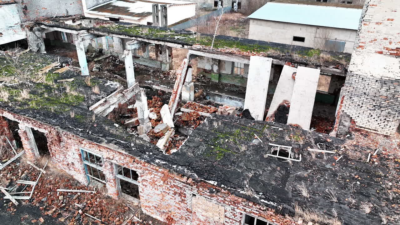 Fully ruined building with no roof or windows. Scattered bricks, beams and pieces of concrete from a premise after armed conflict. Aerial view.