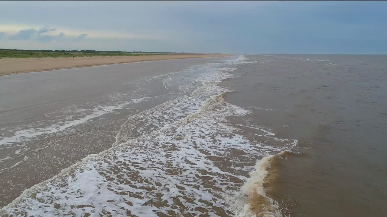 un vuelo de avión no tripulado de bajo nivel por una hermosa playa de la costa este en el reino unido, mientras que la marea entrante se lava en la playa