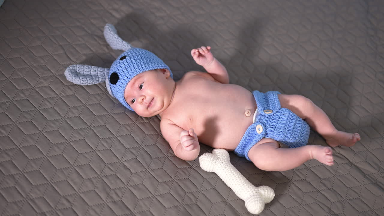 Adorable baby in costume of a puppy on the bed. Kid lying and moving his arms and legs quickly. Cute child yawning.