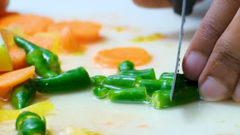 chef cortando pimienta verde en primer plano con algunas zanahorias en el fondo y jugo de verduras en la superficie blanca