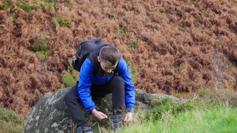 young boy sitting and resting, fastening his walking boots, in a autumn outdoors landscape scene