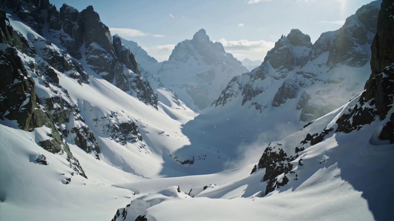 La telecamera inizia a scendere in un passo alpino con neve che cade, rivelando una cima distante