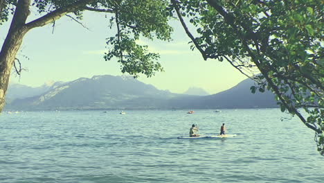 people boating on lake annecy, third largest lake in france, peaceful and sunny day, with a mountain landscape background