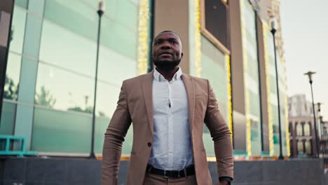 A-confident-man-with-Black-skin-a-short-haircut-and-a-beard-is-persistently-waiting-for-his-colleague-who-is-late-for-a-meeting-in-the-city-and-looks-at-his-watch