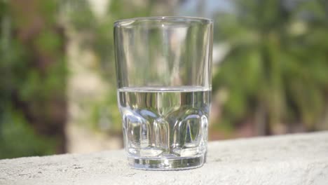 Glass-half-filled-with-water-isolated-against-an-out-of-focus-background,-closeup,-slow-raise-and-tilt,-4K