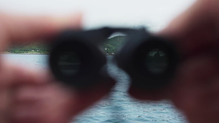 Dita che tengono un mini binocolo in riva all'acqua