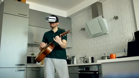 joven feliz bailando y tocando la guitarra en la cocina usando auriculares vr 360 y lo siente guitarrista en concierto en casa