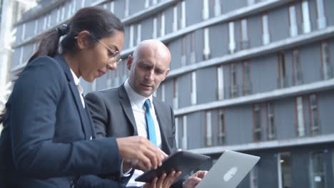 side view of business colleagues watching and discussing project on tablet outside